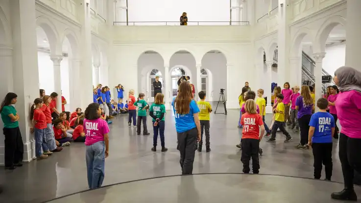 Die Kinder befinden sich nun in einem weißen Saal mit floral verzierten Säulen, Rundbögen und erhöhter Galerie.