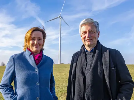 Auf einer Wiese stehen die beiden Gründer von OurPower vor einem Windrad.