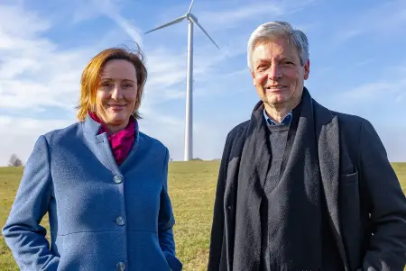 Auf einer Wiese stehen die beiden Gründer von OurPower vor einem Windrad.