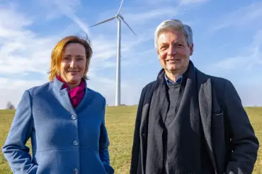 Auf einer Wiese stehen die beiden Gründer von OurPower vor einem Windrad.