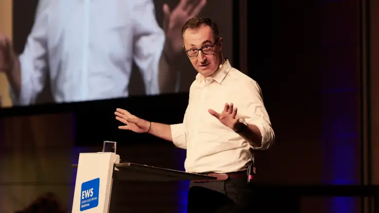 Ein Mann, Cem Özdemir, steht an einem Podium und spricht, die Hände ausgebreitet.