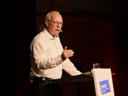 Ein Mann, Thomas Jorberg, steht an einem Podium und spricht, eine Hand ausgestreckt.