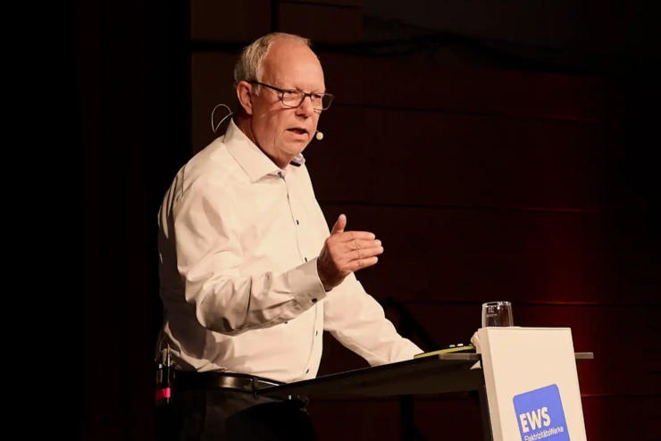 Ein Mann, Thomas Jorberg, steht an einem Podium und spricht, eine Hand ausgestreckt.