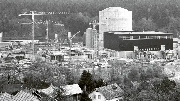 Eine Schwarz-Weiß-Auf¬nah¬me zeigt eine Baustelle: zwischen Stahl und Beton zeichnen sich die typischen Konturen eines Reaktorblocks ab.