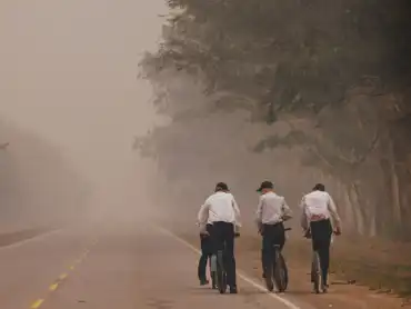 Vier Männer in Einheitskluft befahren mit ihren Rädern eine Straße, die scheinbar nach wenigen Metern in dichtem Qualm endet.