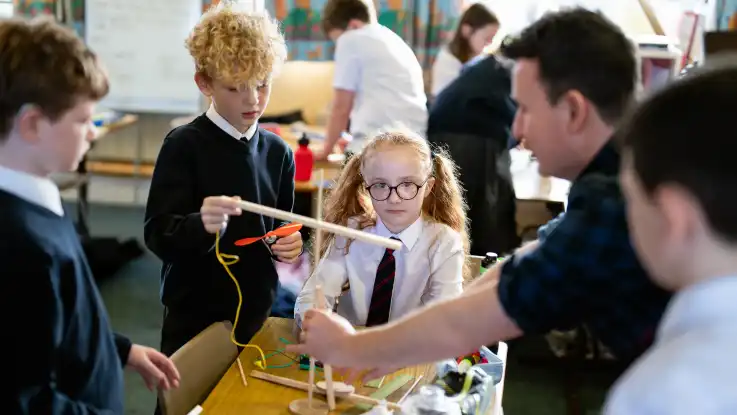 An einem weiteren Tisch werkeln Jungen und Mädchen in Schuluniformen an einer Miniatur-Windkraftanlage. 