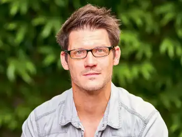 Porträtaufnahme: Ein Mann mittleren Alters mit kurzen, dunkelblonden Haaren und rechteckiger Brille schaut mit wachem Blick zur Kamera. 