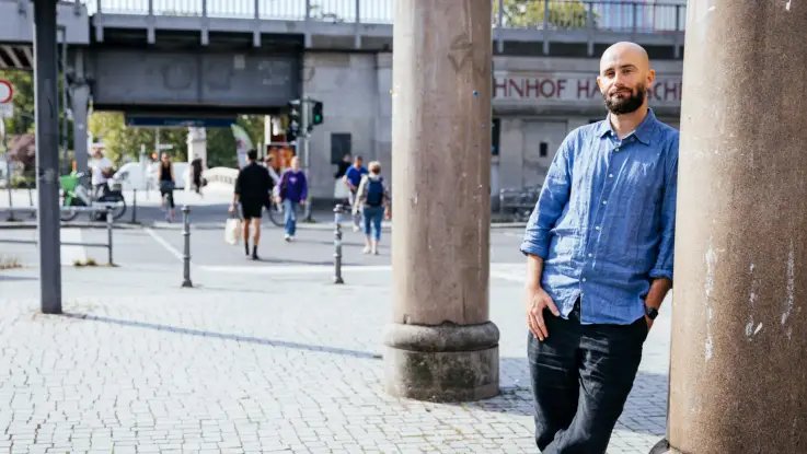 Philipp Staab lehnt in sommerlicher Kleidung an einer Säule vor einer städtischen Straßenszene.