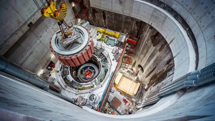 Blick in einen breiten, betonierten Schacht: auf der Baustelle am Grund werden technische Gerätschaften montiert. 