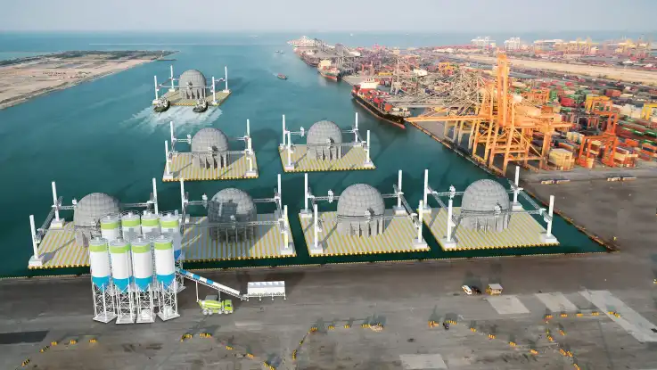 Ein bearbeitetes Bild zeigt sieben haushohe Betonkugeln, die auf floßartigen Konstruktionen in einem Industriehafen stehen. 