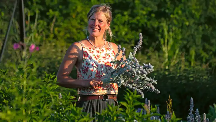 Eine jungen Frau mit einem frischen Sonnenteint hält einen Blumenstraß in Händen udn lacht in die Kamera.