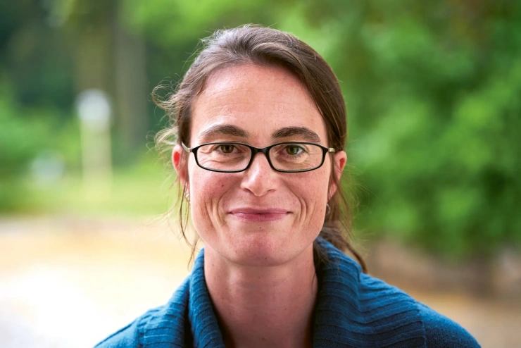 Porträtaufnahme: Eine junge Frau hat ihre braunen Haare zum Zopf gebunden und trägt eine Brille mit rechteckigen Gläsern. 