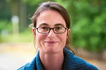 Porträtaufnahme: Eine Frau mittleren Alters hat ihre braunen Haare zum Zopf gebunden und trägt eine Brille mit rechteckigen Gläsern. 