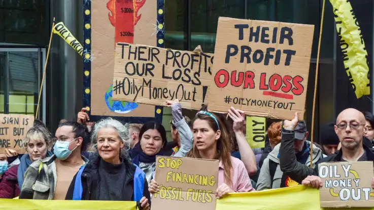Eine Gruppe protestiert mit handgeschriebenen Schildern, auf einem ist zu lesen: Stop financing fossil fuels.