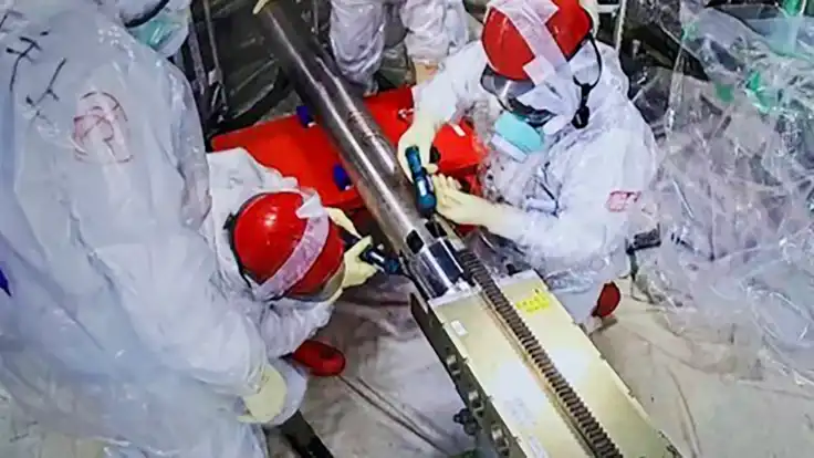 Vier Männer in Schutzkleidung und roten Helmen arbeiten auf engsten Raum an einer rohrförmigen Apparatur. 