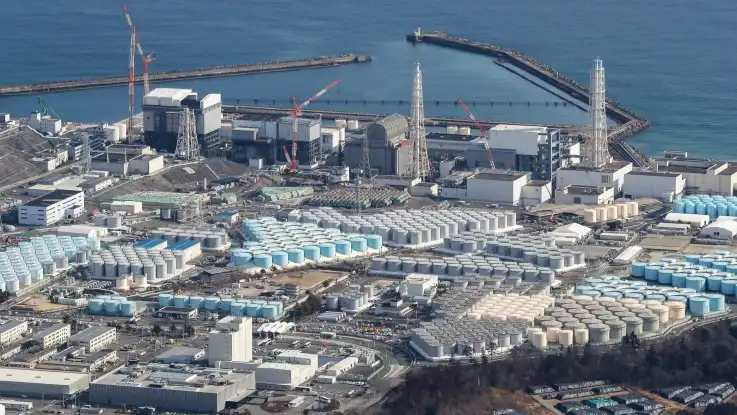 Luftaufnahme: Überall auf dem Werksgelände stehen riesige Wassertanks, hinter den Reaktorhallen beginnt das Meer. 
