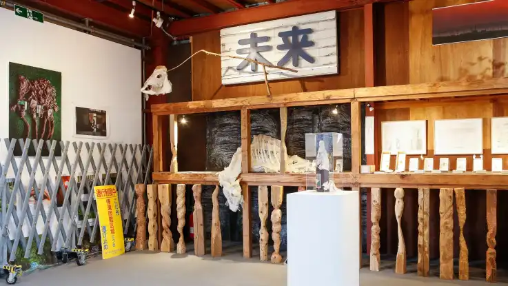 In einer Ecke stehen Ausstellungstücke: Schilder mit japanischen Schriftzeichen, Holzschnitzereien und Alltagsgegenstände. 