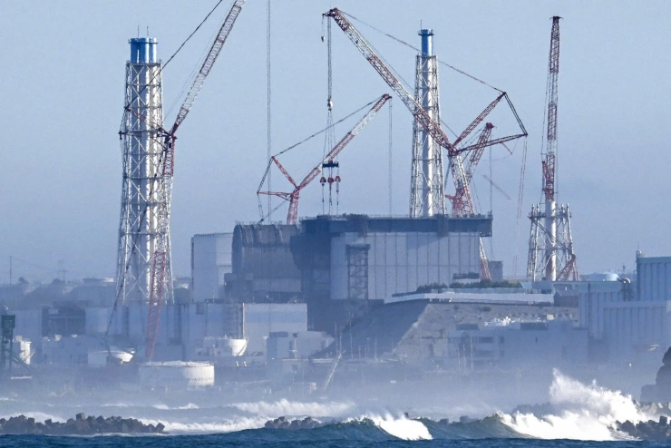  Aus einer mit Wellenbrechern versehenen Brandung ragt die riesenhafte Silhouette eines Atomkraftwerks empor.