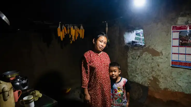 In einer anderen Hütte posiert eine Mutter mit ihrem Sohn im Grundschulalter, hinter ihnen hängen Maiskolben zum Trocknen. 