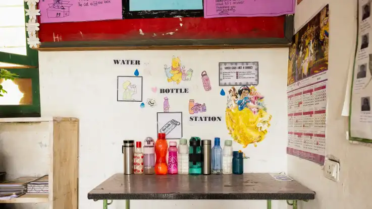 Im Inneren eines Klassenraums stehen Wasserflaschen auf einem Tisch. An der Wand darüber steht „water bottle station“.  