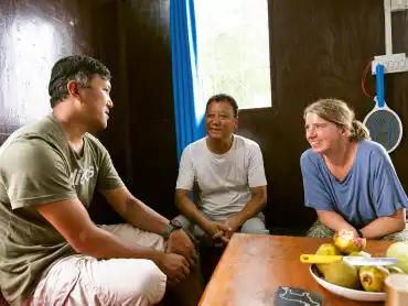 Zwei Männer und eine Frau sitzen an einem Holztisch und unterhalten sich angeregt. 