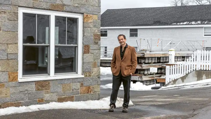 Jon Ippolito steht lässig auf dem Gehweg einer winterlichen Kleinstadt-Straße und schaut in die Kamera.