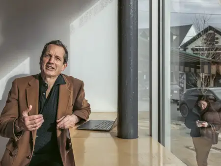 Jon Ippolito spricht in die Kamera, während draußen auf der Straße eine Frau vorübergeht, die in ihr Smartphone schaut.