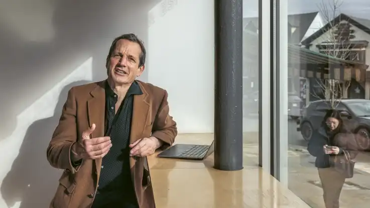 Jon Ippolito spricht in die Kamera, während draußen auf der Straße eine Frau vorübergeht, die in ihr Smartphone schaut.