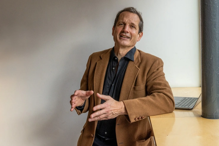 Jon Ippolito spricht gestikulierend in die Kamera, während er an einem Stehtisch lehnt. 