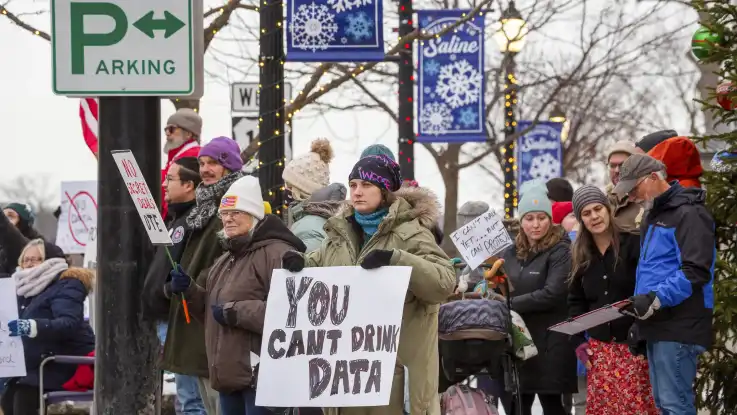 Demonstrierende haben sich bei winterlichem Wetter an einer Straße versammelt. Auf einem Schild ist zu lesen: „You cant drink data“.