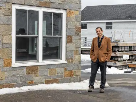 Jon Ippolito steht lässig auf dem Gehweg einer winterlichen Kleinstadt-Straße und schaut in die Kamera.