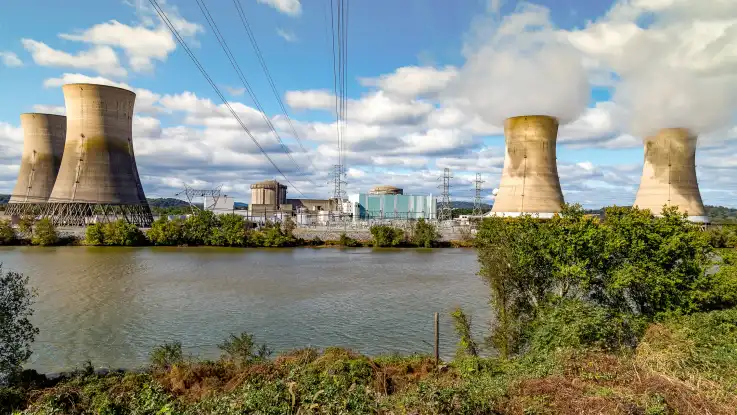 Ein Atomkraftwerk erstreckt sich entlang eines Flussufers. Aus zwei der vier Kühltürme wabert gräulicher Wasserdampf. 