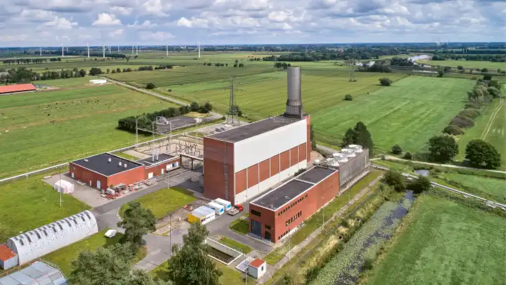 Schräg von oben: Ein industriell geprägter Gebäudekomplex mit rechteckigen Bauwerken samt Umschlagwerk und Schornstein.  