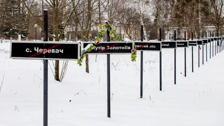 Kreuzförmige Schilder mit durchgestrichenen Ortsnamen in kyrillischer Schrift stehen in einer langen Reihe.