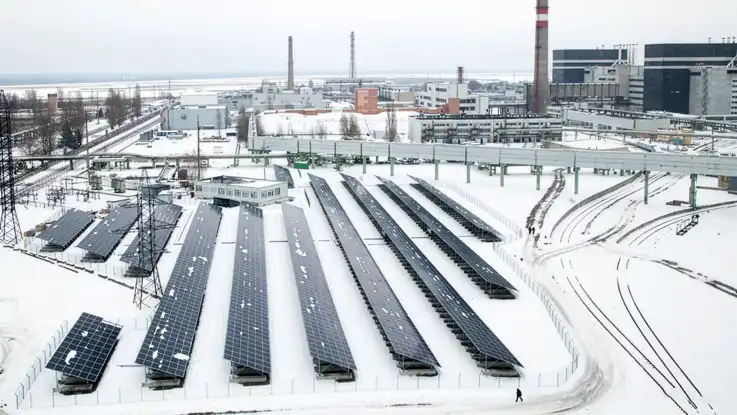 Eine Aufnahme aus erhöhter Position zeigt mehrere Reihen von Photovoltaik-Modulen, die am Rand des Werksgeländes stehen.