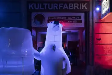 Junges Paar, das bei Nacht vor dem großen Veranstaltungseingang einen Eisblock bestaunt.