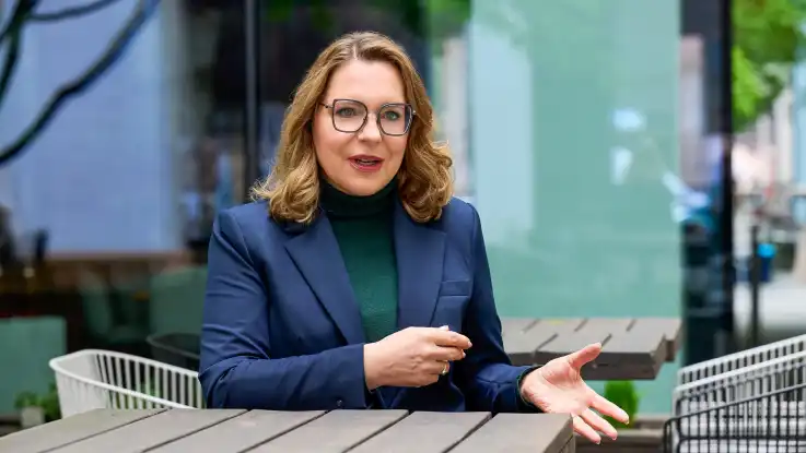 Claudia Kemfert sitzt an einem Holztisch in einer städtischen Umgebung und spricht mit einem gegenüber, das nicht im Bil dist.äölsd#fkd#gödlkh