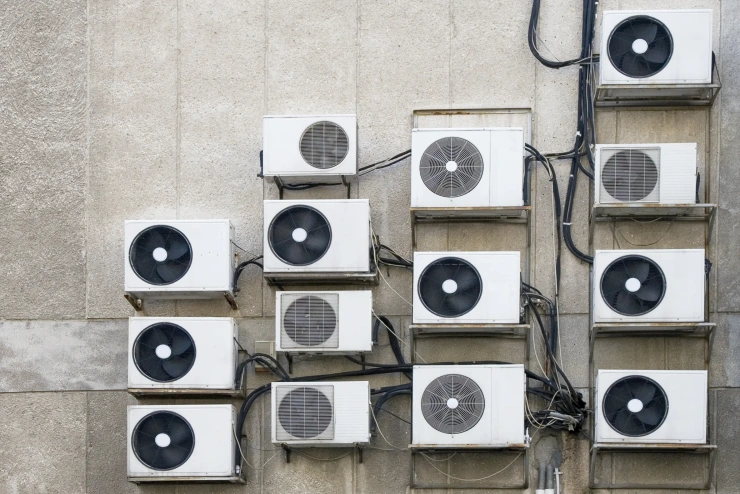 Einige Klimaanlagen mit schwarzen Stromkabeln hängen vor einer grauen Brandmauer. 