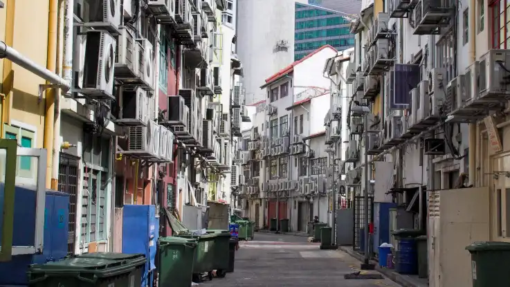 Vor den Häuserfassaden in einer schmalen, menschenleeren Gasse hängen hunderte Klimaanlagen. 