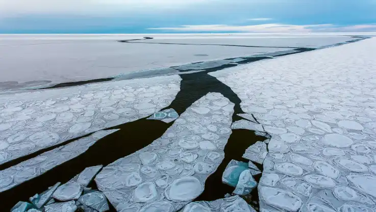 Eine weitere Landschaftsaufnahme zeigt ebenfalls weitläufige Eisflächen, doch das Eis ist deutlich dünner – stellenweise wird es von Meerwasser durchbrochen.