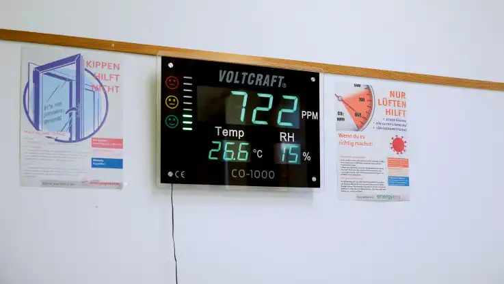 An einer weißen Wand hängt eine schwarze elektronische Anzeigetafel mit mehreren digitalen leuchtenden Anzeigefeldern.