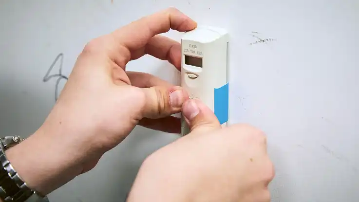 Nahaufnahme der Installation des Messgerätes an der Heizung, die dort mit Klebeband befestigt wird.