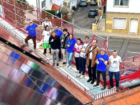 Auf einer Plattform neben einer Dach-PV-Fläche steht eine Gruppe von etwa 15 Personen.