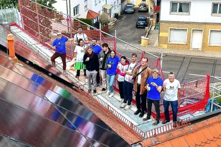 Auf einer Plattform neben einer Dach-PV-Fläche steht eine Gruppe von etwa 15 Personen.