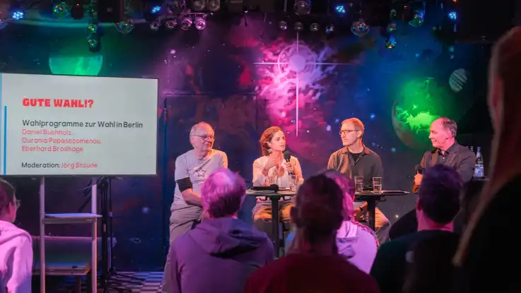 Podiumsdiskussion mit vier Personen vor Publikum und Bildschirm mit Text zu Wahlprogrammen in Berlin.